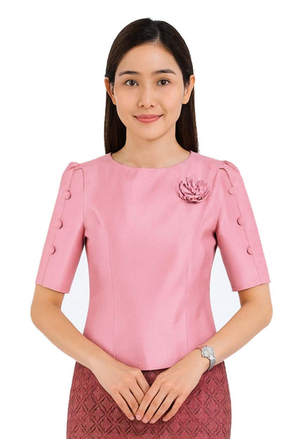 May include: A short-sleeved pink blouse featuring a round neckline, a fabric flower embellishment on the left chest, and three decorative buttons aligned vertically along the outer edge of each sleeve, paired with a textured dark red skirt.