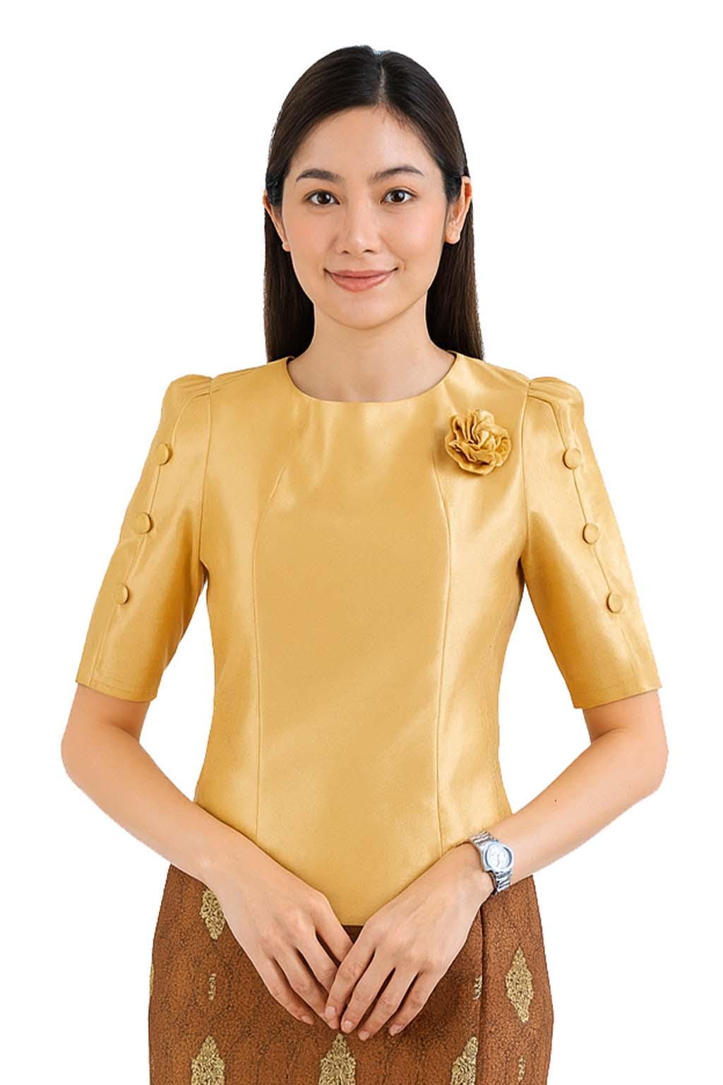 May include: A gold-colored blouse with a round neckline, short sleeves featuring three buttons on each side, and a matching fabric flower pinned to the left chest. The blouse is paired with a brown skirt featuring a gold-toned patterned design.