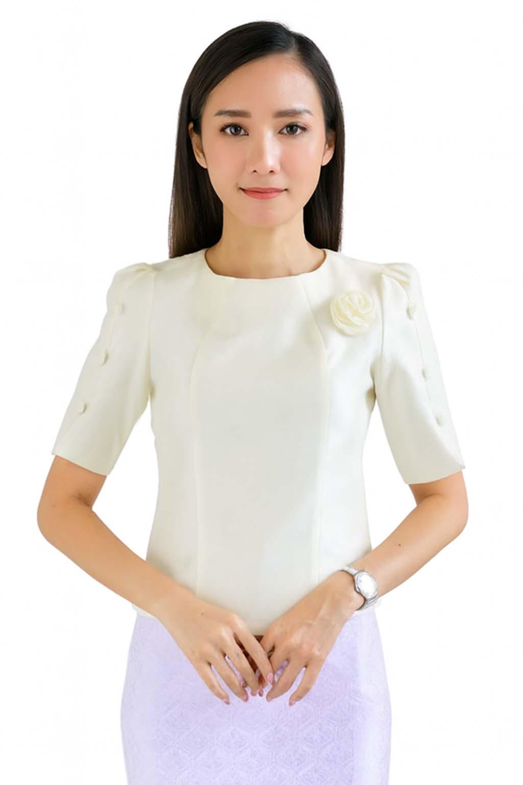 May include: A cream-colored short-sleeved blouse featuring a round neckline, puff sleeves with three decorative buttons on each side, and a fabric flower accent on the left chest. The blouse is paired with a light purple skirt with a subtle pattern.