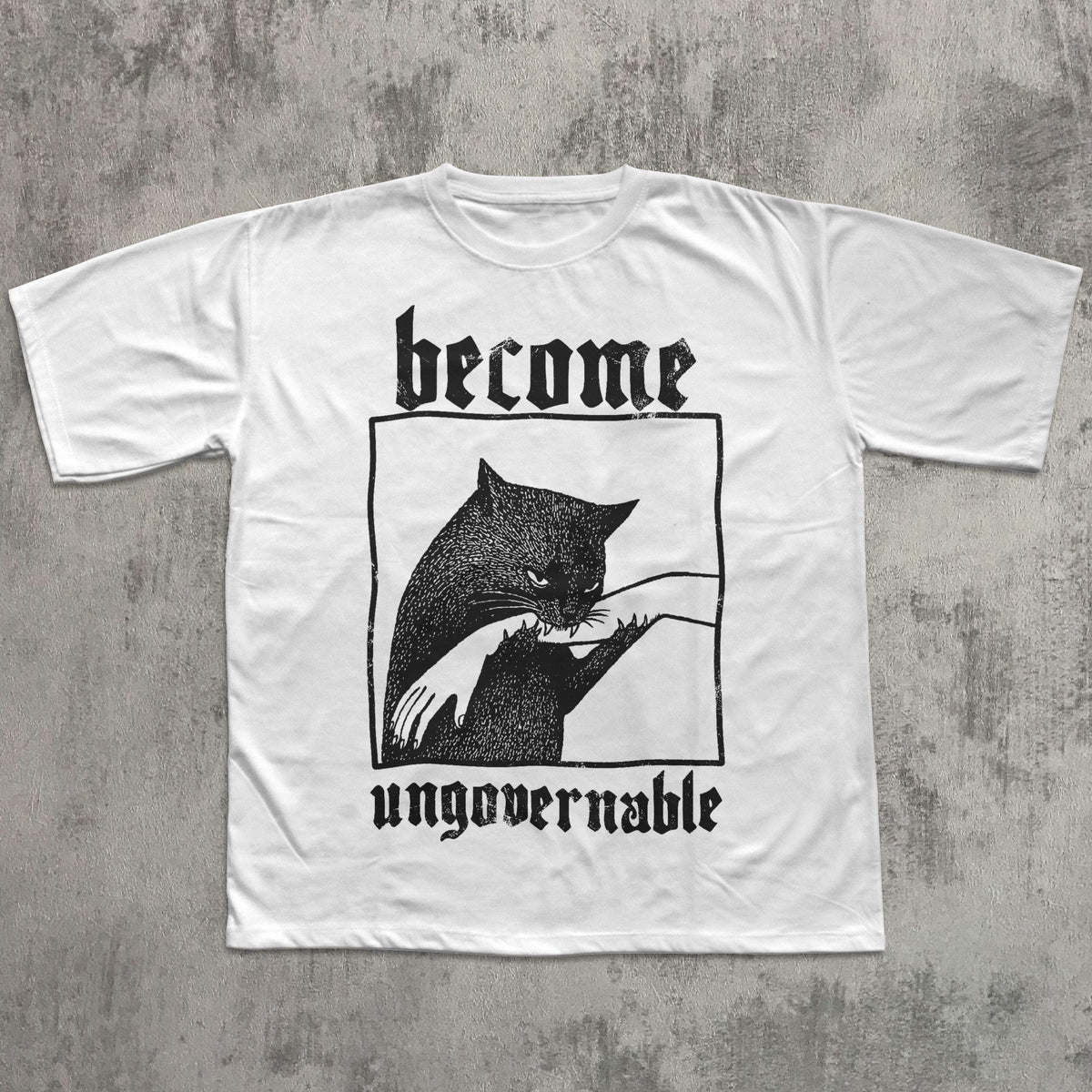 May include: White t-shirt with a black graphic of a cat biting a hand, framed within a black rectangle. The words "become" and "ungovernable" are printed above and below the graphic in a gothic font.