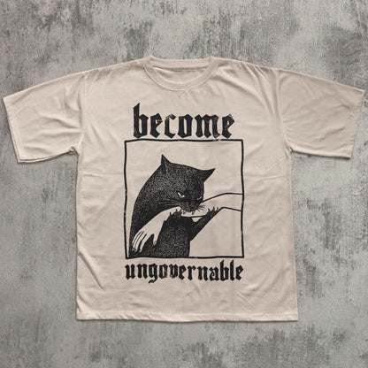 May include: Cream-colored t-shirt featuring a black graphic of a cat biting a hand, framed within a rectangle. The words "become" and "ungovernable" are printed above and below the graphic in a gothic font.