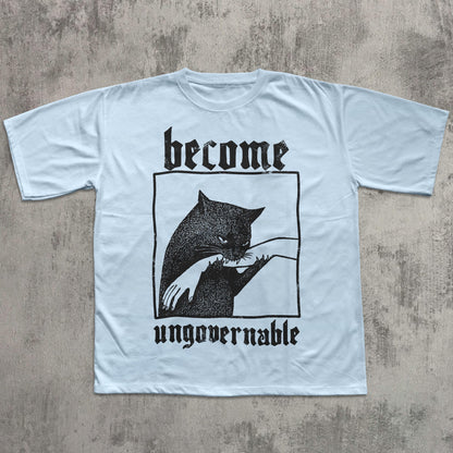 May include: Light blue t-shirt with a black graphic of a cat biting a hand, inside a black rectangle. The word "become" is above the graphic, and "ungovernable" is below, in a gothic font.