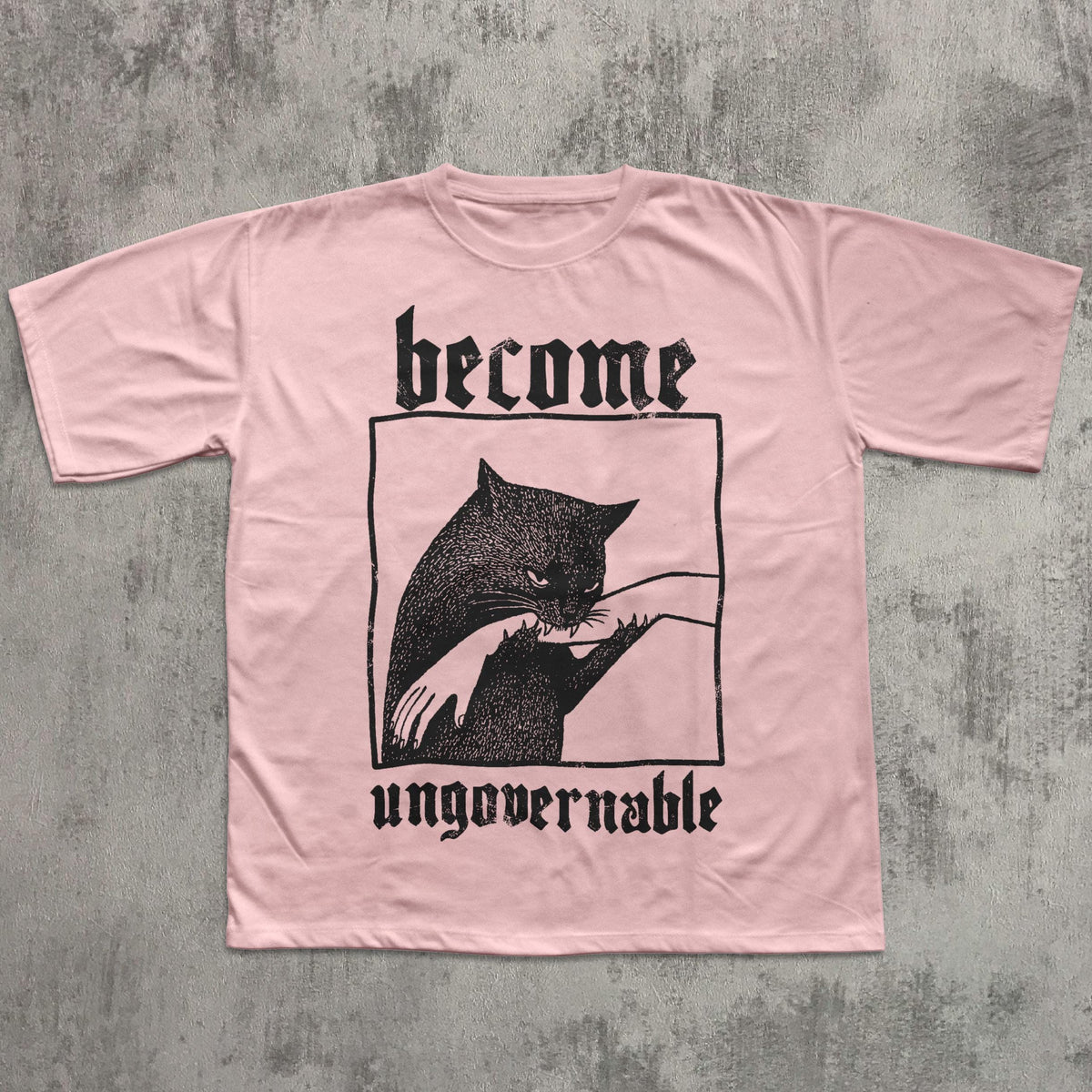 May include: A light pink t-shirt featuring a black graphic of a cat biting a hand, framed within a black rectangle. The words "become" and "ungovernable" are printed above and below the graphic in a gothic font.