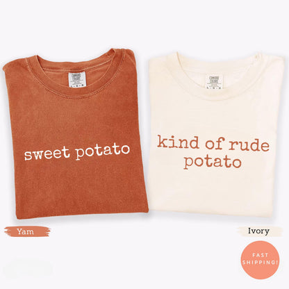 May include: Two folded t-shirts, one burnt orange and one ivory. The burnt orange shirt reads "sweet potato" in white text. The ivory shirt reads "kind of rude potato" in brown text. Both shirts have a crew neck.