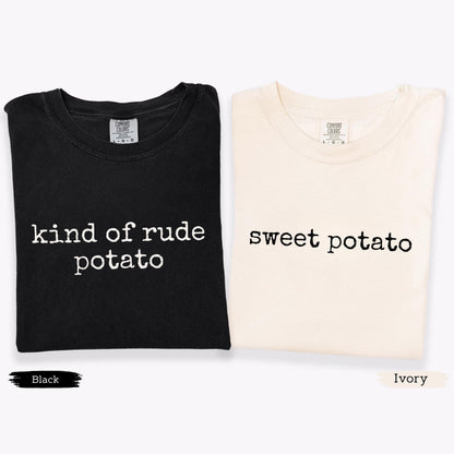 May include: Two t-shirts, one black and one ivory, are displayed. The black shirt has the text "kind of rude potato" in white, while the ivory shirt says "sweet potato" in black. Both shirts have a crew neck and short sleeves.