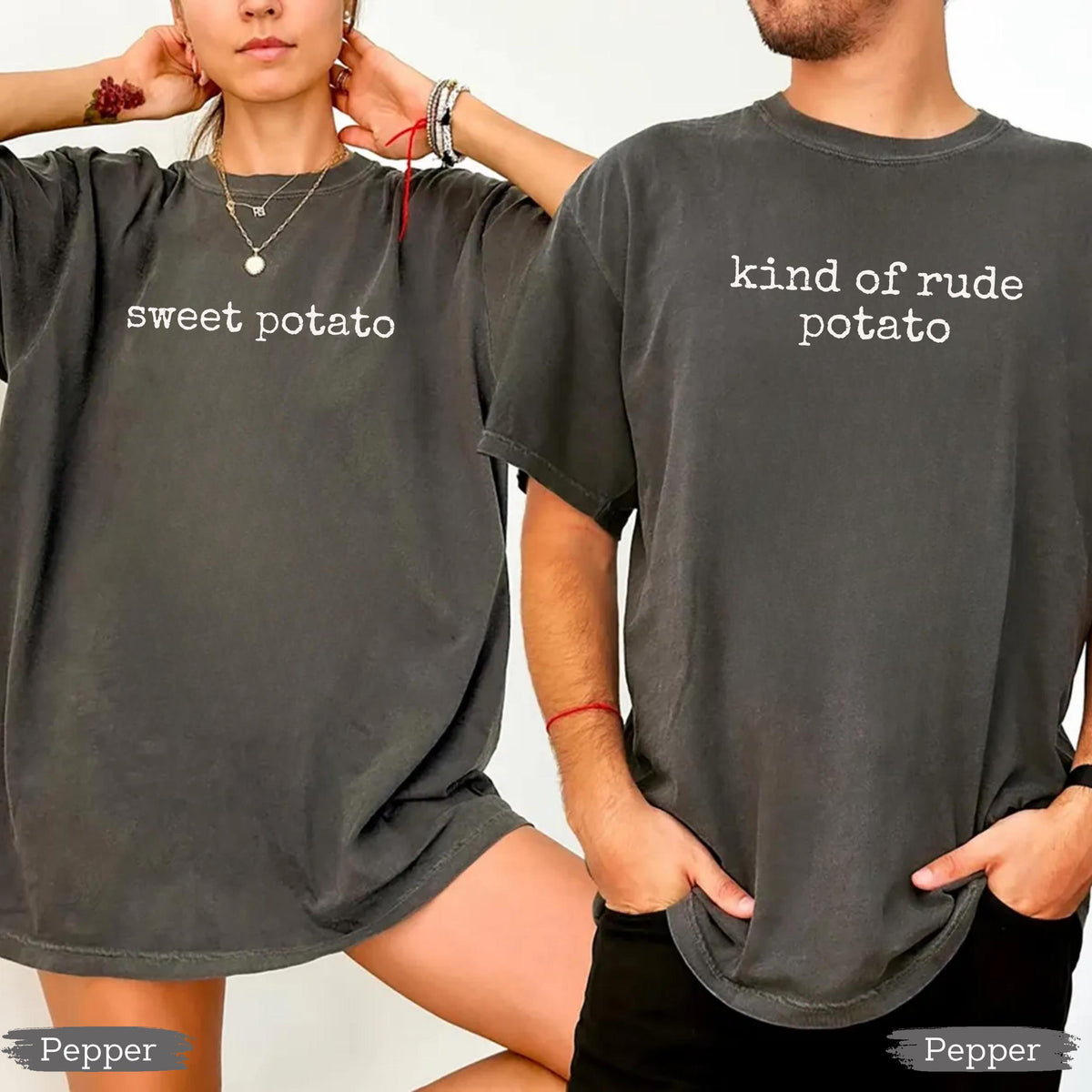 May include: Two dark gray t-shirts with white text. One shirt says "sweet potato" and the other says "kind of rude potato". The shirts are short-sleeved and have a vintage, worn look.