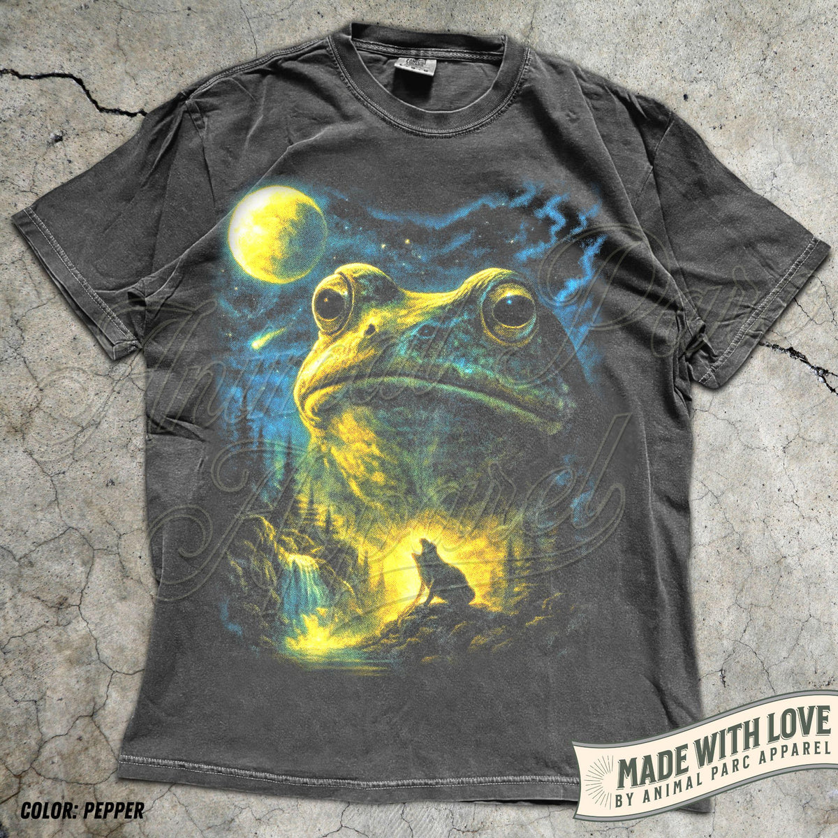 May include: A charcoal gray short-sleeve t-shirt featuring a large graphic print of a giant frog head above a forest landscape with a howling wolf, a waterfall, and a bright yellow moon in a starry night sky. The shirt has a crew neckline.