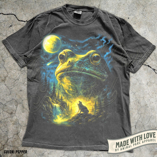 May include: A charcoal gray short-sleeve t-shirt featuring a large graphic print of a giant frog head above a forest landscape with a howling wolf, a waterfall, and a bright yellow moon in a starry night sky. The shirt has a crew neckline.