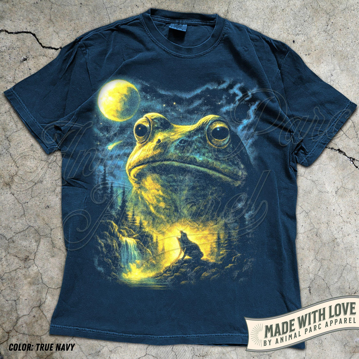 May include: A true navy short-sleeve t-shirt featuring a graphic print of a large frog head above a forest landscape with a waterfall, a glowing yellow moon, and a silhouette of a howling wolf against a starry night sky background.
