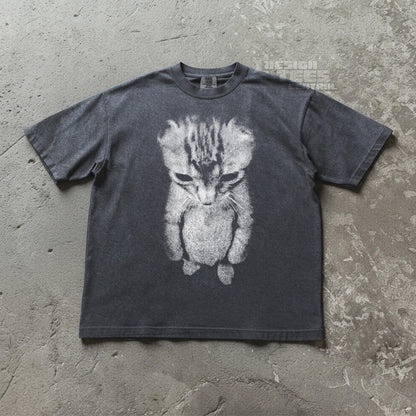 May include: Dark gray t-shirt featuring a distressed, grayscale image of a kitten. The kitten is depicted with a downward gaze, creating a melancholic expression. The shirt has short sleeves and a crew neck. The text "DESIGN TEES CONTROL" is visible on the upper right.