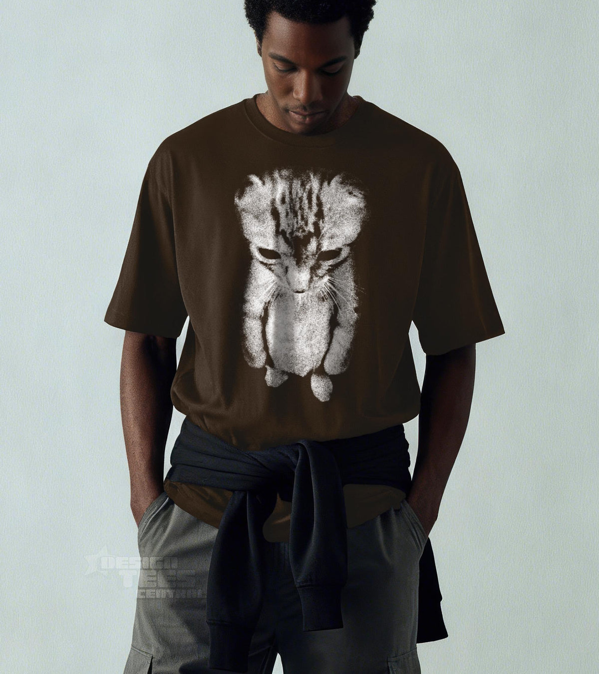 May include: A brown t-shirt featuring a grayscale illustration of a sad-looking kitten. The cat is depicted in a stylized, almost sketch-like manner, with its head bowed. The shirt has short sleeves and a crew neck.