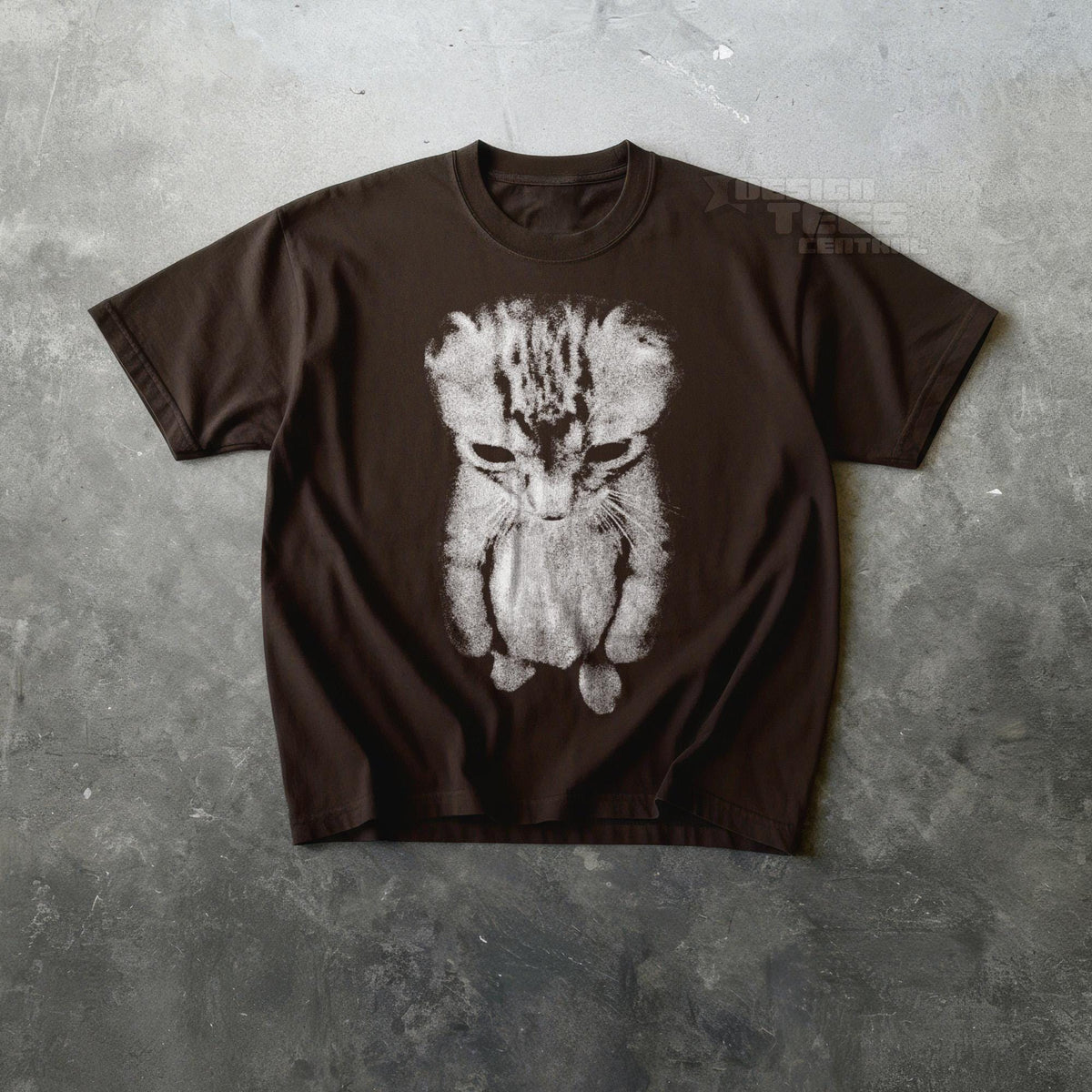 May include: A brown t-shirt featuring a distressed, grayscale image of a sad-looking cat. The cat's face and body are depicted in a stylized, almost sketch-like manner, with a focus on its downturned eyes and posture.