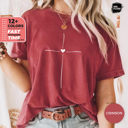 May include: A crimson short-sleeved t-shirt featuring a white line-art cross graphic with a small heart at the center. The shirt is worn with a brown leather belt and a layered gold necklace. Text on the image includes 12+ COLORS, FAST PROCESSING TIME, INK FLOW, and CRIMSON.