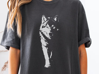 May include: Dark gray t-shirt featuring a white graphic of a wolf. The wolf is depicted in a detailed, artistic style, with a focus on its face and front legs. The shirt has short sleeves and a relaxed fit.