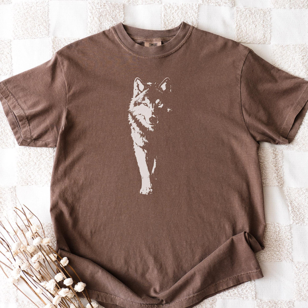 May include: A brown t-shirt featuring a white graphic of a wolf. The wolf is depicted in a stylized, minimalist design, with the animal's head and front legs visible. The shirt has short sleeves and a crew neck.