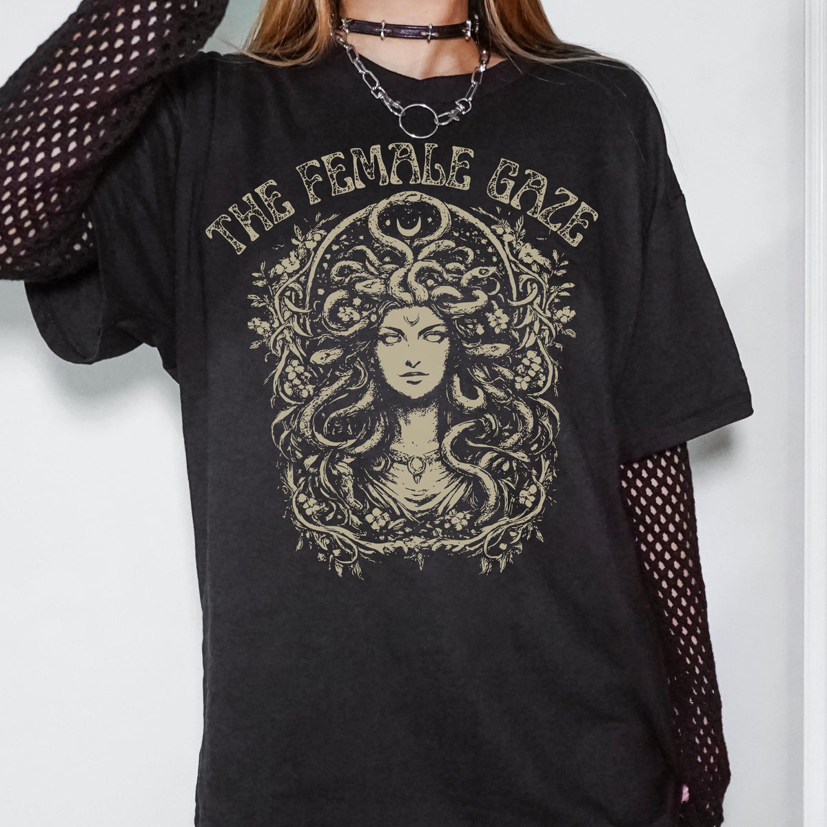 May include: Black t-shirt featuring a Medusa illustration with the text "THE FEMALE GAZE" in a vintage style. The graphic is in shades of beige and tan. The shirt has short sleeves and a relaxed fit.