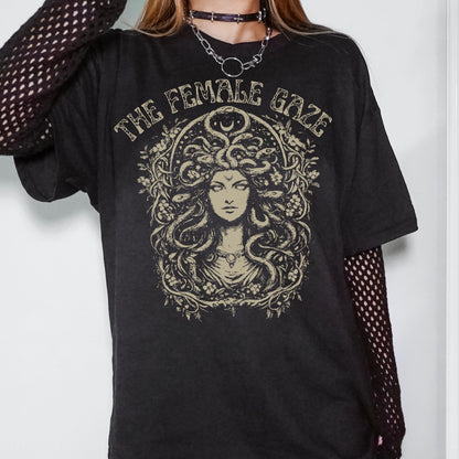 May include: Black t-shirt featuring a Medusa illustration with the text "THE FEMALE GAZE" in a vintage style. The graphic is in shades of beige and tan. The shirt has short sleeves and a relaxed fit.