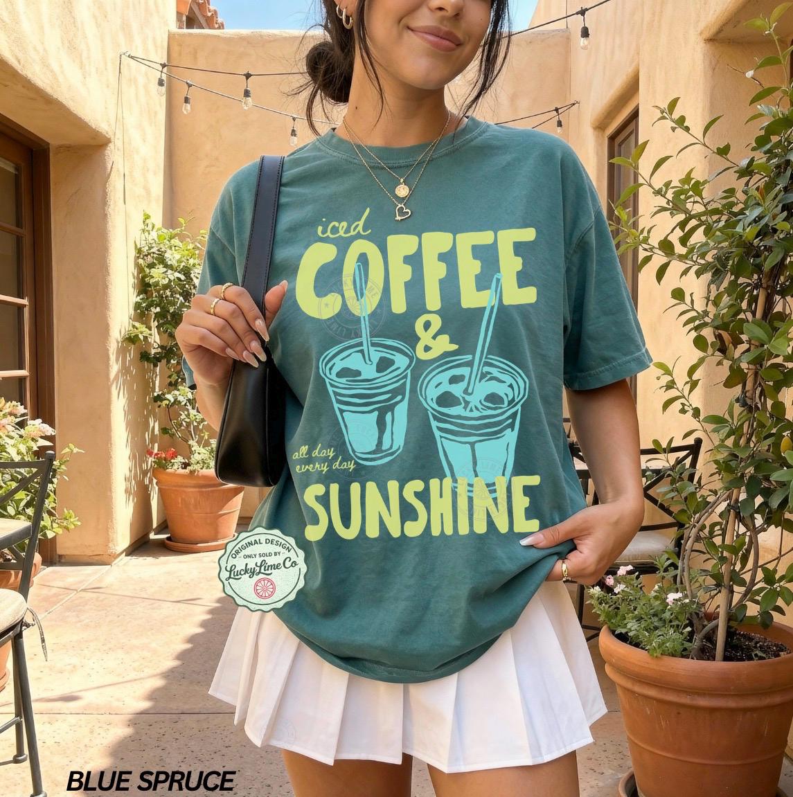 May include: Blue spruce t-shirt with the text "iced COFFEE & SUNSHINE" and two coffee cup illustrations in light blue and yellow. The shirt also has the text "all day every day". The shirt is paired with a white pleated skirt.