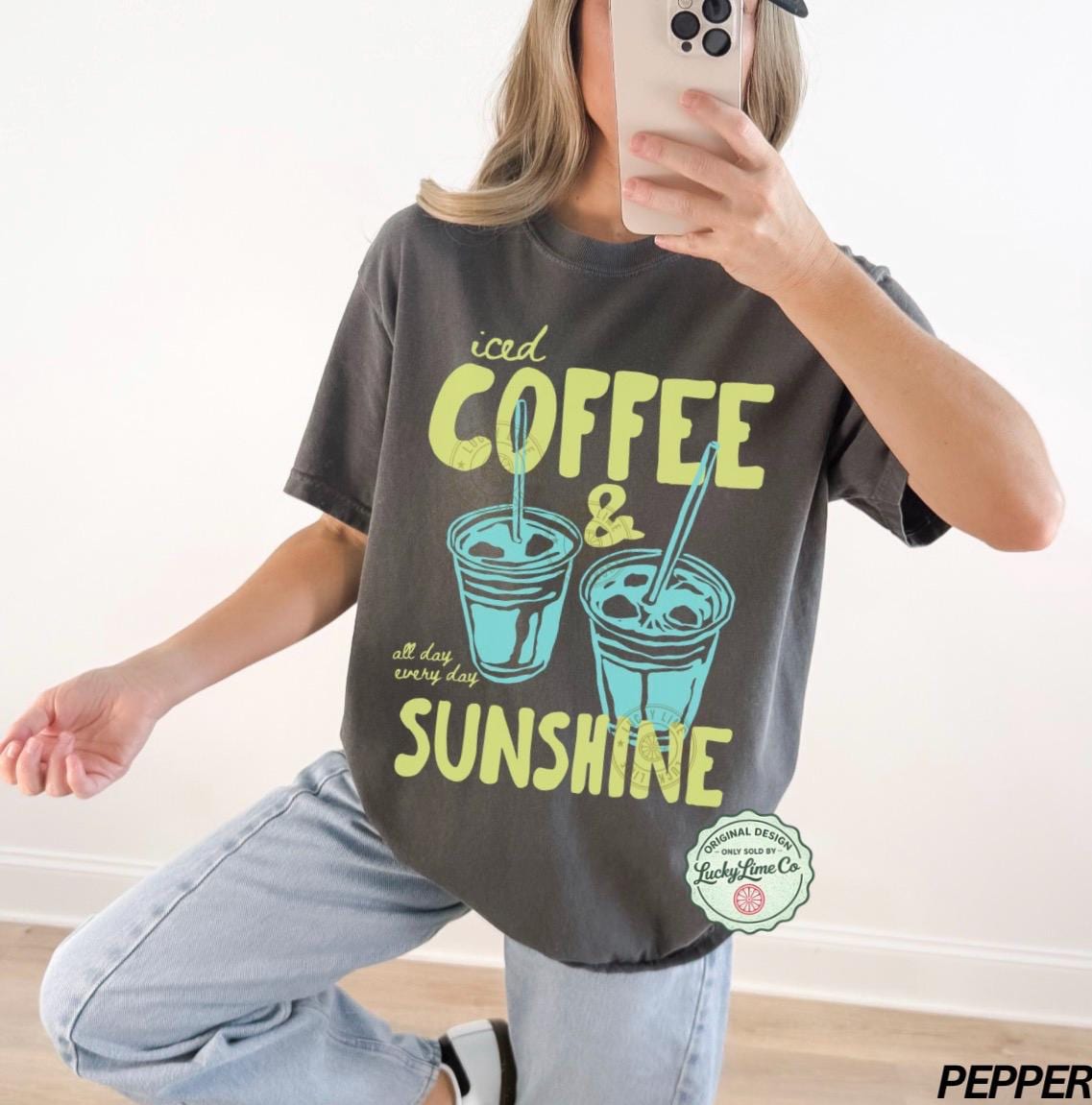 May include: Dark gray t-shirt with the words "iced COFFEE & SUNSHINE" in yellow and teal. The shirt features two iced coffee cup illustrations. The text "all day every day" is also included.