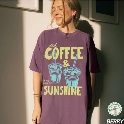 May include: Berry-colored t-shirt with the words "iced COFFEE & SUNSHINE" in a retro font. The graphic includes two iced coffee cups with straws. The shirt also has the text "all day every day".