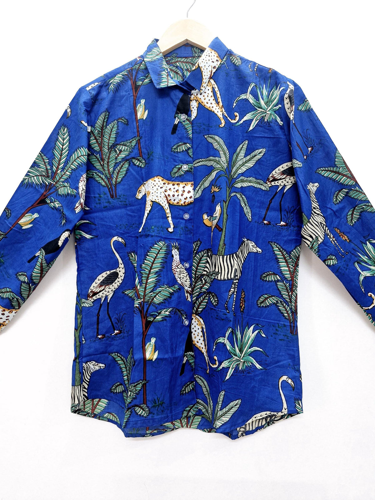 May include: A long-sleeved blue button-down shirt with a vibrant jungle print. The design features leopards, zebras, birds, and palm trees. The shirt is made of a lightweight fabric and is displayed on a wooden hanger.