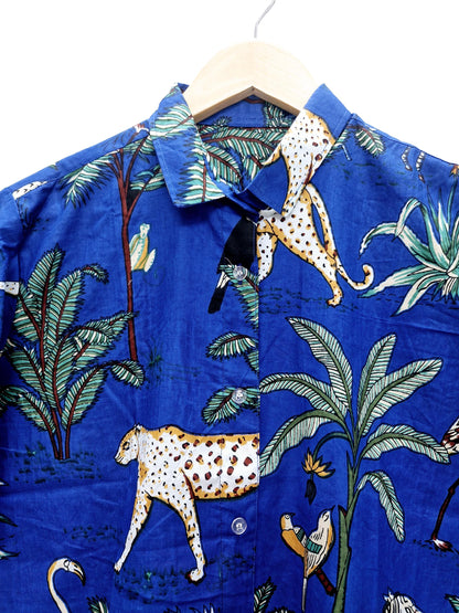 May include: A blue button-down shirt with a tropical print featuring leopards, palm trees, and birds. The shirt is hanging on a wooden hanger. The fabric has a crinkled texture.