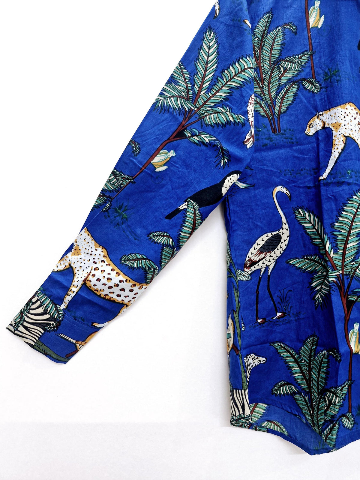 May include: A long-sleeved blue shirt with a vibrant jungle print. The design features leopards, zebras, toucans, and flamingos amidst palm trees. The shirt's fabric has a slight sheen, enhancing the vivid colors of the animal and plant illustrations.