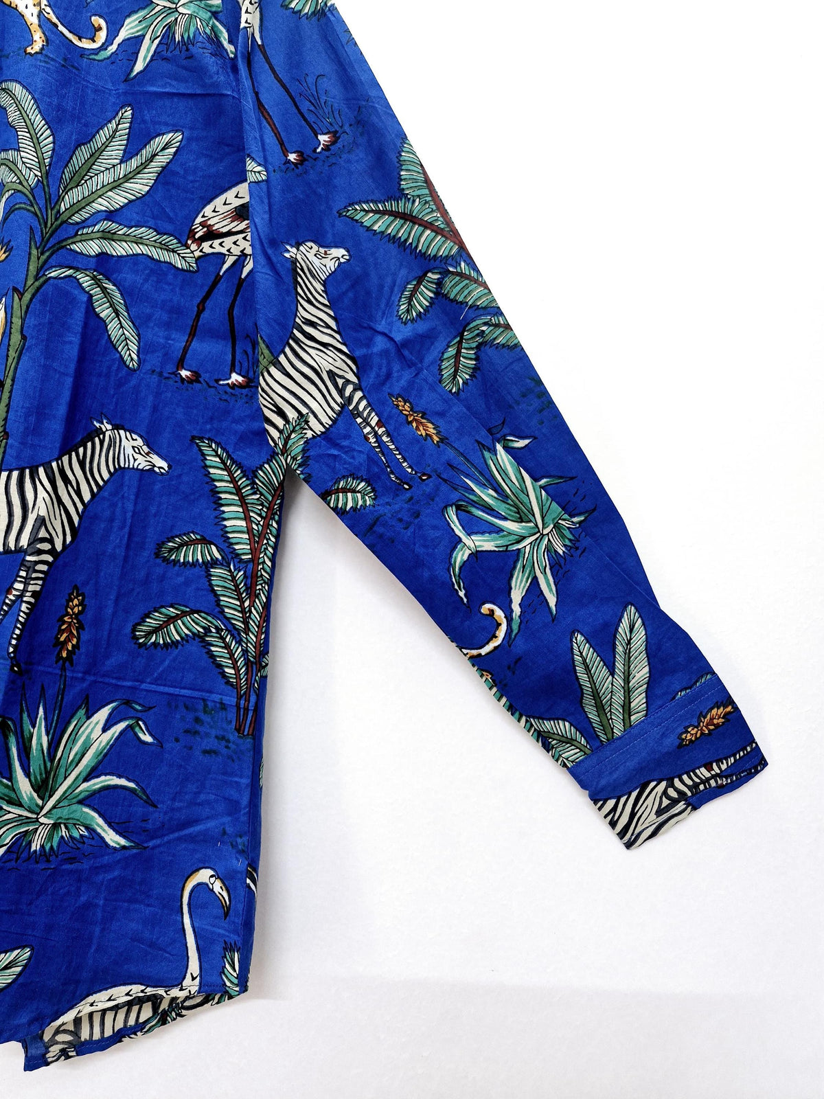 May include: A long-sleeved blue shirt featuring a vibrant safari print. The design includes zebras, flamingos, and lush tropical foliage. The shirt's sleeve is visible, showcasing the detailed pattern and the cuff.