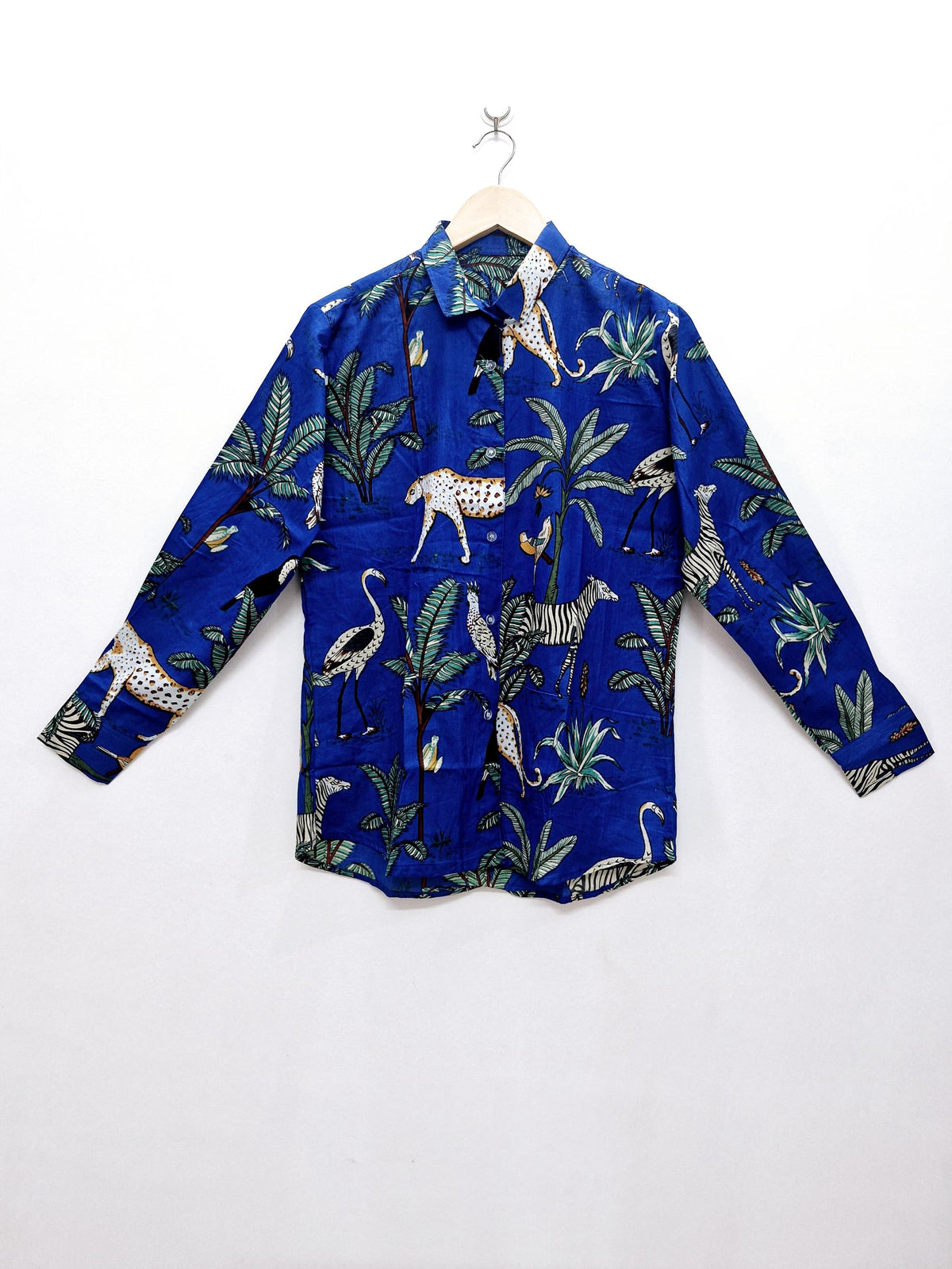 May include: A long-sleeved blue shirt with a jungle animal print. The shirt features zebras, leopards, and birds among green foliage. The shirt is hanging on a wooden hanger against a white background.