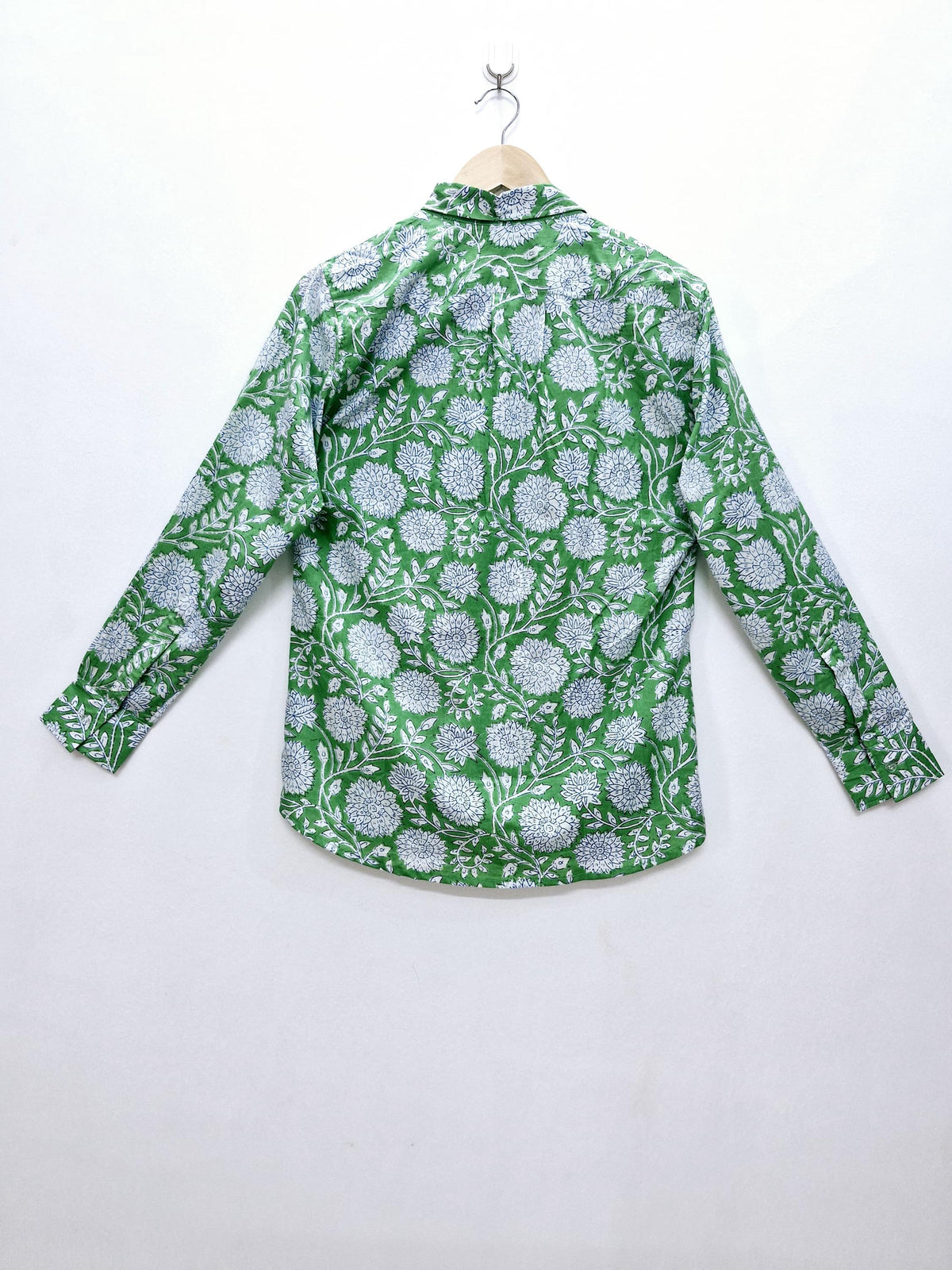 May include: Green button-down shirt with a white floral pattern. The long-sleeved shirt is hanging on a wooden hanger against a white background. The floral design covers the entire shirt.