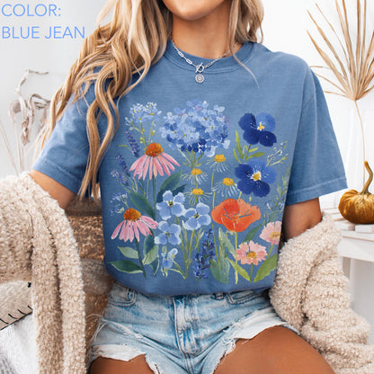 May include: Blue jean colored t-shirt featuring a watercolor floral design with pink, blue, and orange flowers. The shirt has short sleeves and a crew neck. The text "COLOR: BLUE JEAN" is in the upper left corner.