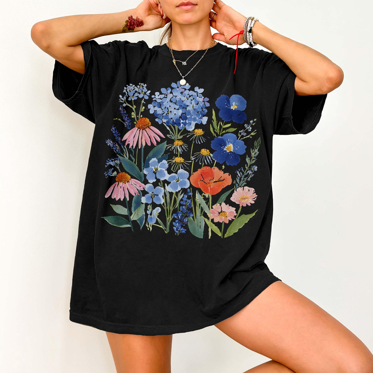 May include: Black t-shirt featuring a vibrant floral design. The graphic showcases a bouquet of colorful flowers, including blue hydrangeas, pink coneflowers, and red poppies. The shirt is a comfortable, oversized fit.