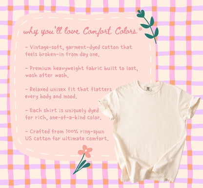 May include: Cream-colored Comfort Colors t-shirt on a pink and orange plaid background. The image includes text describing the shirt's features: vintage-soft cotton, heavyweight fabric, relaxed fit, and unique dye.