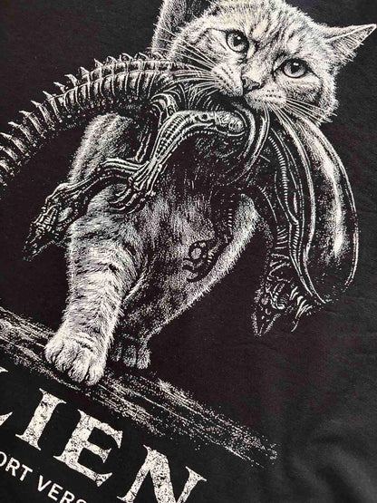 May include: A black t-shirt featuring a white graphic illustration of a cat carrying a xenomorph creature in its mouth. The design includes the partial text "IEN" and "ORT VER" in a distressed white font at the bottom of the printed graphic.