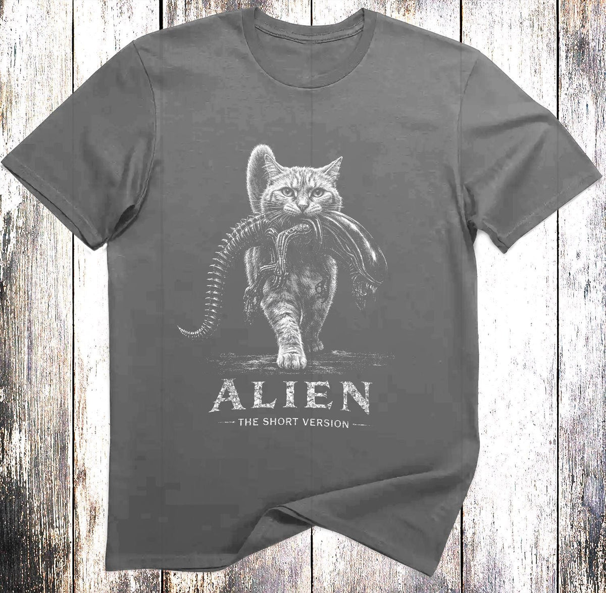 May include: A charcoal gray short-sleeved t-shirt featuring a white graphic of a cat carrying a xenomorph creature in its mouth. Below the illustration, the text reads ALIEN THE SHORT VERSION in a distressed white font centered on the chest.