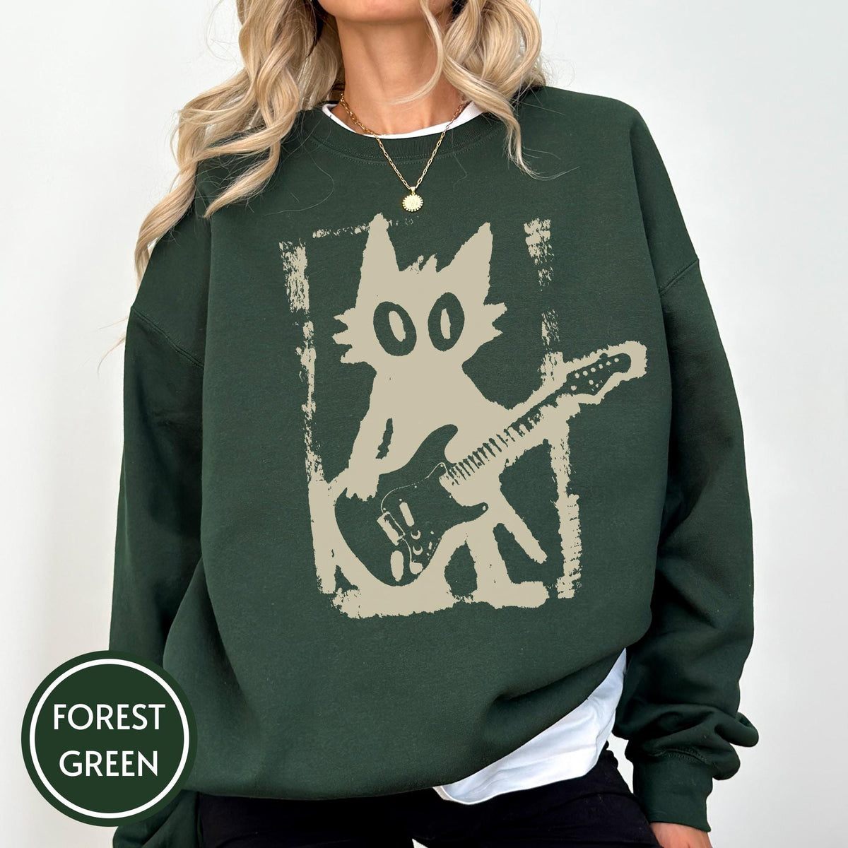 May include: A forest green long-sleeve sweatshirt featuring a beige graphic print of a stylized cat playing an electric guitar. The design is framed by a distressed rectangular border. The sweatshirt has a crew neckline and ribbed cuffs.