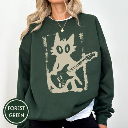 May include: A forest green long-sleeve sweatshirt featuring a beige graphic print of a stylized cat playing an electric guitar. The design is framed by a distressed rectangular border. The sweatshirt has a crew neckline and ribbed cuffs.