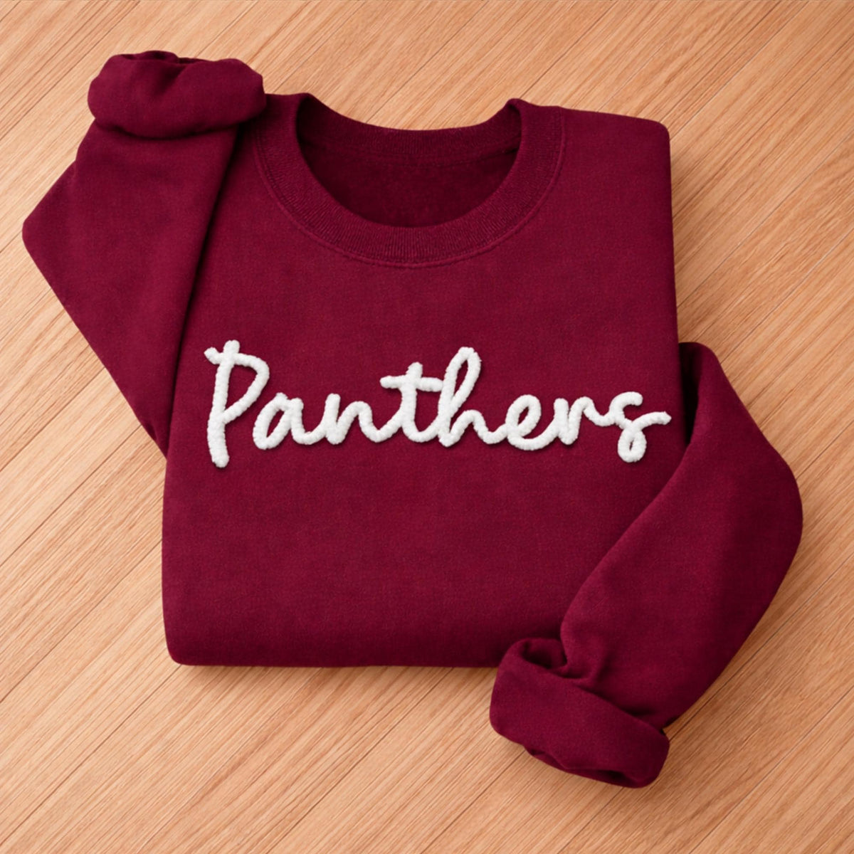 May include: A maroon sweatshirt with the word "Panthers" in white, cursive lettering. The sweatshirt is folded neatly, with the sleeves and collar visible. The fabric appears soft and comfortable.