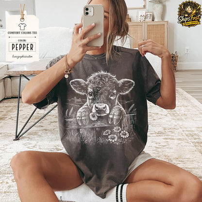 May include: Pepper-colored Comfort Colors tee featuring a graphic of a calf peering over a wooden fence with daisies. The tee has the text "Pepper" and "lunagraphiccustom" on a tag.