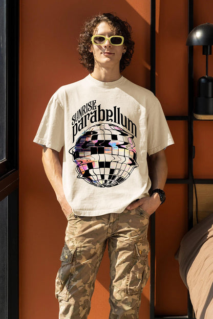 May include: Cream-colored t-shirt with the text "Sunrise Parabellum" above a distorted disco ball graphic. The person is wearing yellow-framed sunglasses and camouflage cargo pants.
