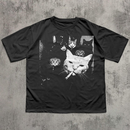 May include: Black t-shirt featuring a graphic of several cats, with one large white cat smoking a cigarette. The other cats are in the background, with various expressions. The design is in black and white.