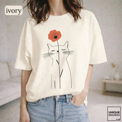May include: An ivory short-sleeve t-shirt featuring a black line art illustration of a cat with closed eyes. A single red poppy flower is positioned above the cat's head, with its stem extending downward in front of the cat's face.