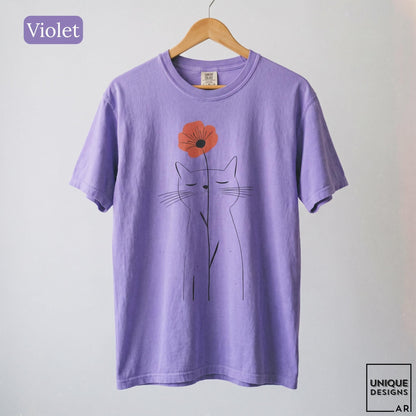 May include: A violet short-sleeve t-shirt featuring a black line art illustration of a cat with closed eyes. A single orange flower is positioned above the cat's head. The text "Violet" appears in the top left corner, and "UNIQUE DESIGNS ARI" is in the bottom right.