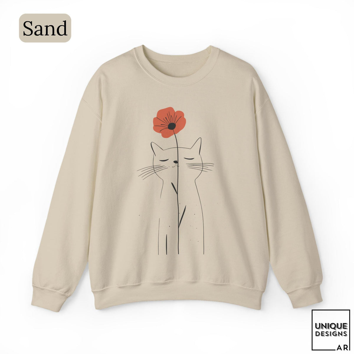 May include: A sand-colored crewneck sweatshirt featuring a black line art illustration of a cat with closed eyes. A single red poppy flower is positioned above the cat's head, with its stem extending downward. The text Sand is in the top left corner.