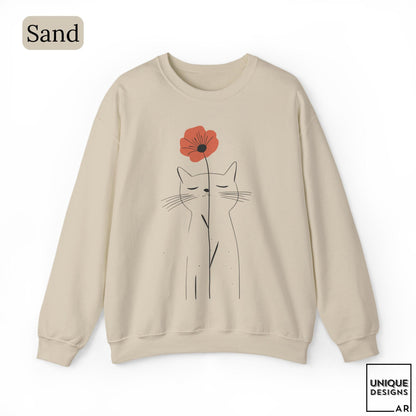 May include: A sand-colored crewneck sweatshirt featuring a black line art illustration of a cat with closed eyes. A single red poppy flower is positioned above the cat's head, with its stem extending downward. The text Sand is in the top left corner.