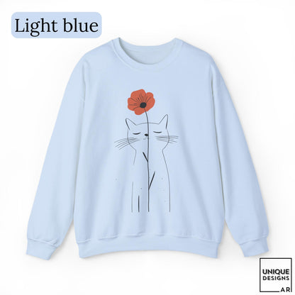 May include: A light blue crewneck sweatshirt featuring a minimalist black line drawing of a cat with closed eyes. A single orange poppy flower is positioned directly above the cat's head. The text "Light blue" appears in the top left corner.
