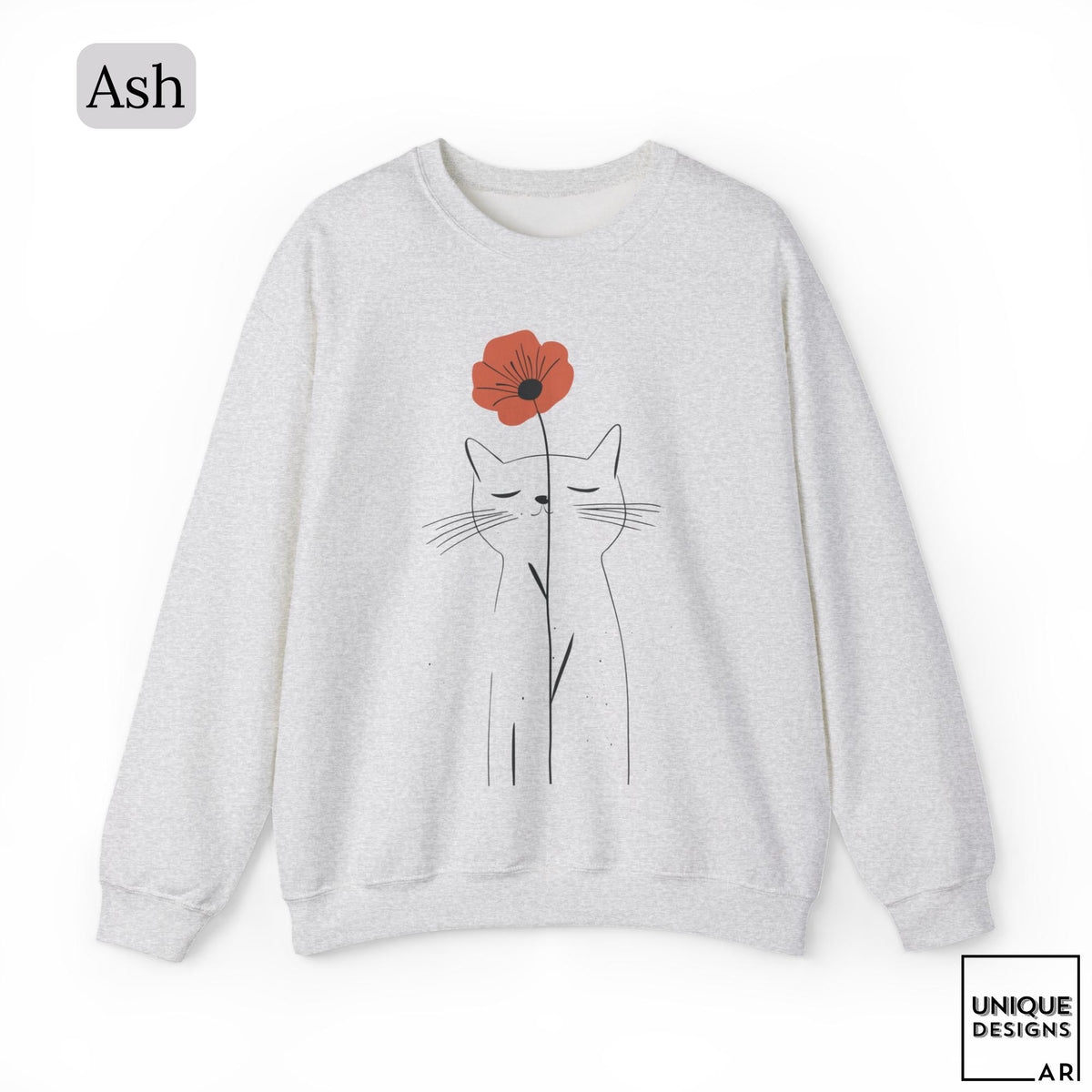 May include: An ash gray crewneck sweatshirt featuring a minimalist black line art illustration of a cat with closed eyes, holding a single red poppy flower. The text Ash appears in the top left corner, and Unique Designs Ari is in the bottom right.