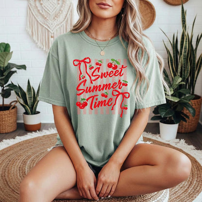 May include: Sage green t-shirt with the text "Sweet Summer Time" in red script and cherries. The design includes red bows and a pink and white striped background. The shirt is a casual, oversized fit.