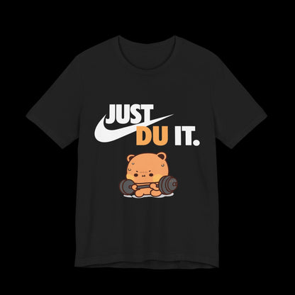 May include: Black t-shirt featuring a cartoon bear lifting weights. The shirt has the text "JUST DU IT." in white and orange, with a white swoosh logo. The bear is orange and brown, with a barbell.