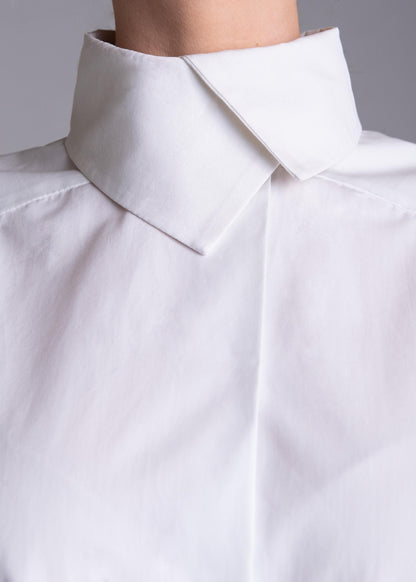 May include: A crisp white button-down shirt featuring a structured high collar with a pointed fold. The garment is made of a smooth, opaque fabric with a clean, minimalist design, showcasing a concealed placket and sharp, tailored shoulder seams.